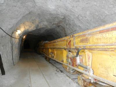 A view inside a rough-hewn underground tunnel or mine shaft featuring a large piece of yellow industrial mining machinery on rails.