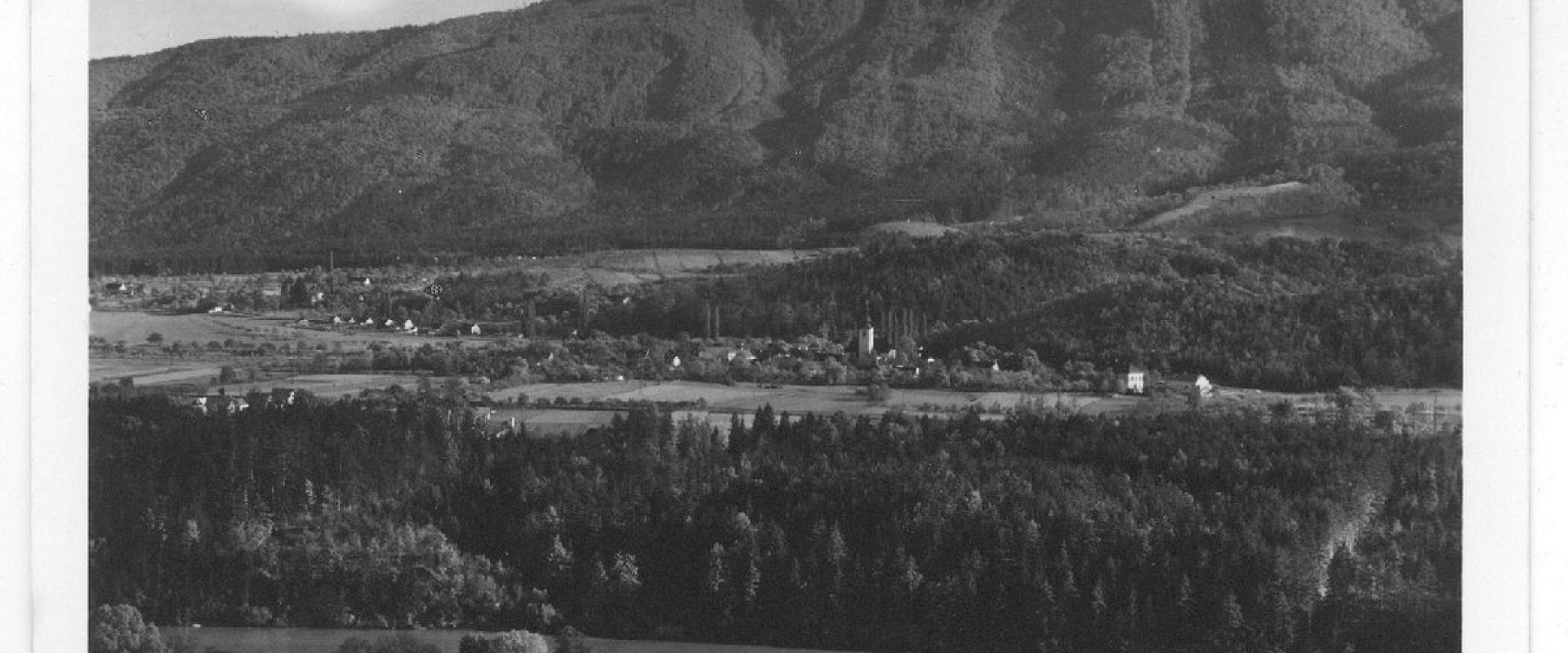 A black and white vintage postcard showing a panoramic view of a village nestled in a valley with a large forested mountain in the background, featuring the handwritten caption "Limbuš pri Mariboru" and a museum stamp.