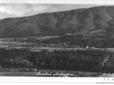 A black and white vintage postcard showing a panoramic view of a village nestled in a valley with a large forested mountain in the background, featuring the handwritten caption "Limbuš pri Mariboru" and a museum stamp.