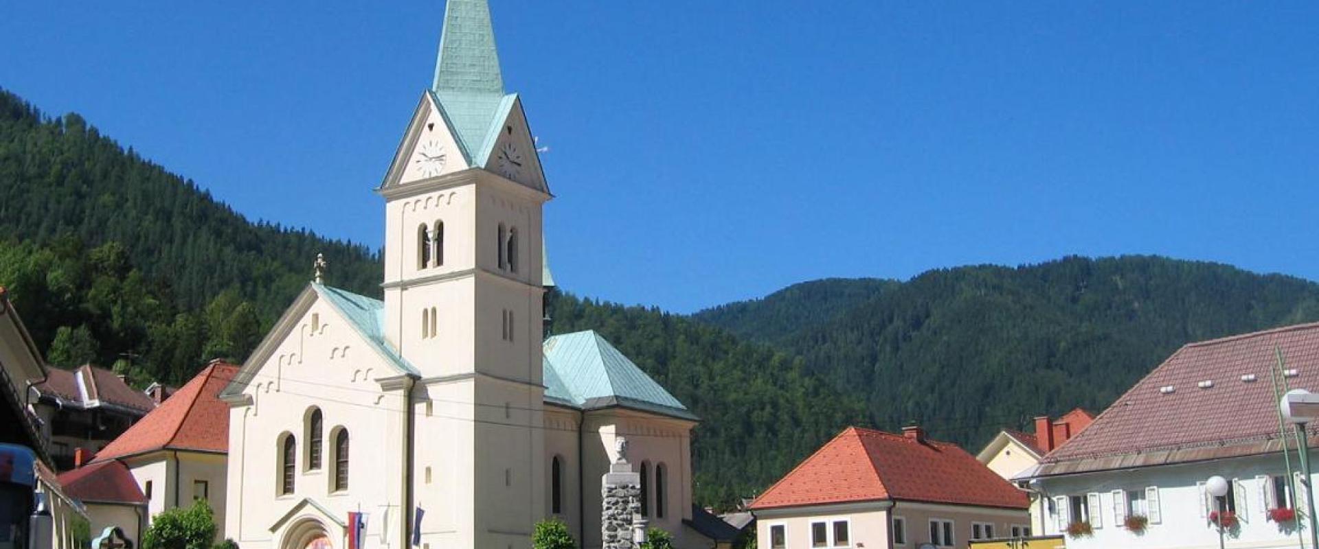 The parish church and village of Črna na Koroškem beneath forested hills