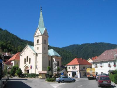 The parish church and village of Črna na Koroškem beneath forested hills