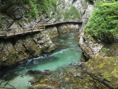 A wooden walkway with railings built along the side of a steep, rocky gorge wall above a clear, turquoise river.